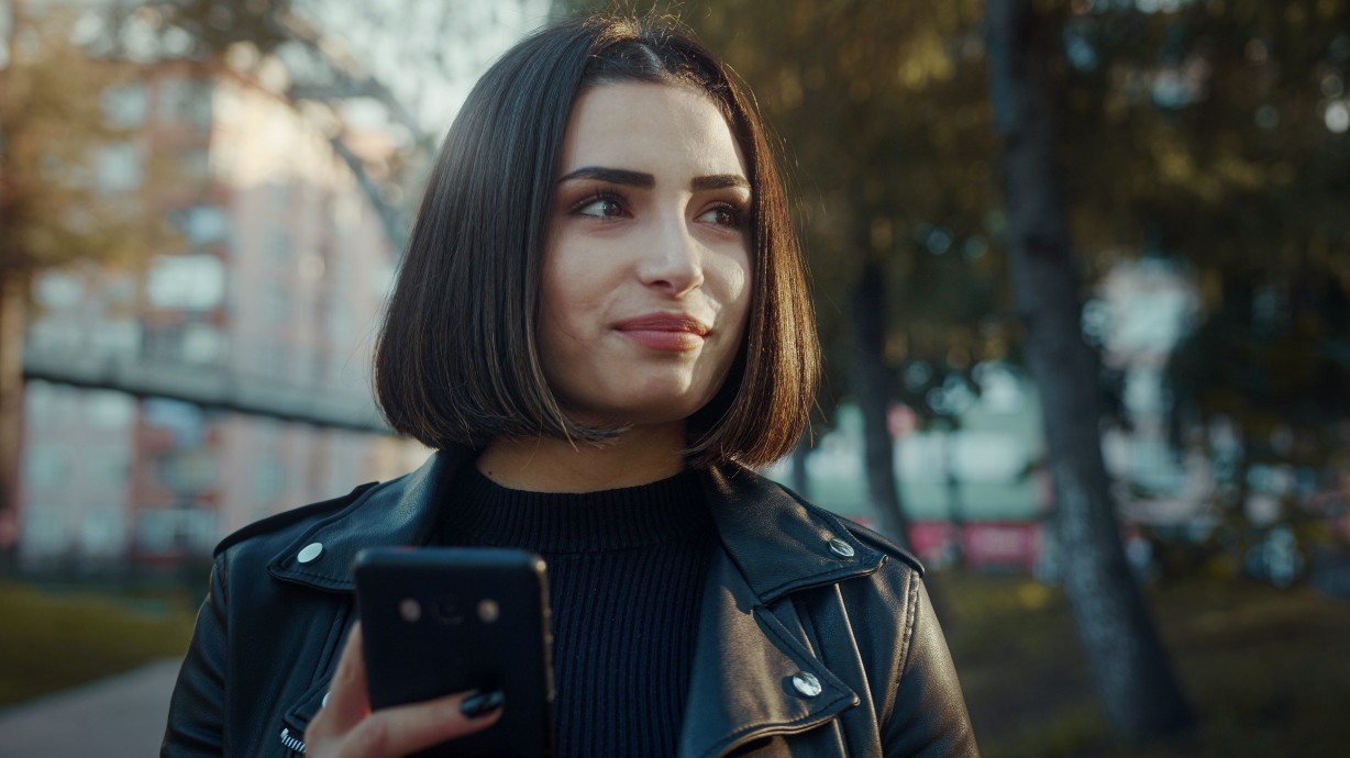 Smiling young woman walking in the park and using smartphone. Enjoying walk. Free time in internet social media. Chatting with friends, typing message, checking email.